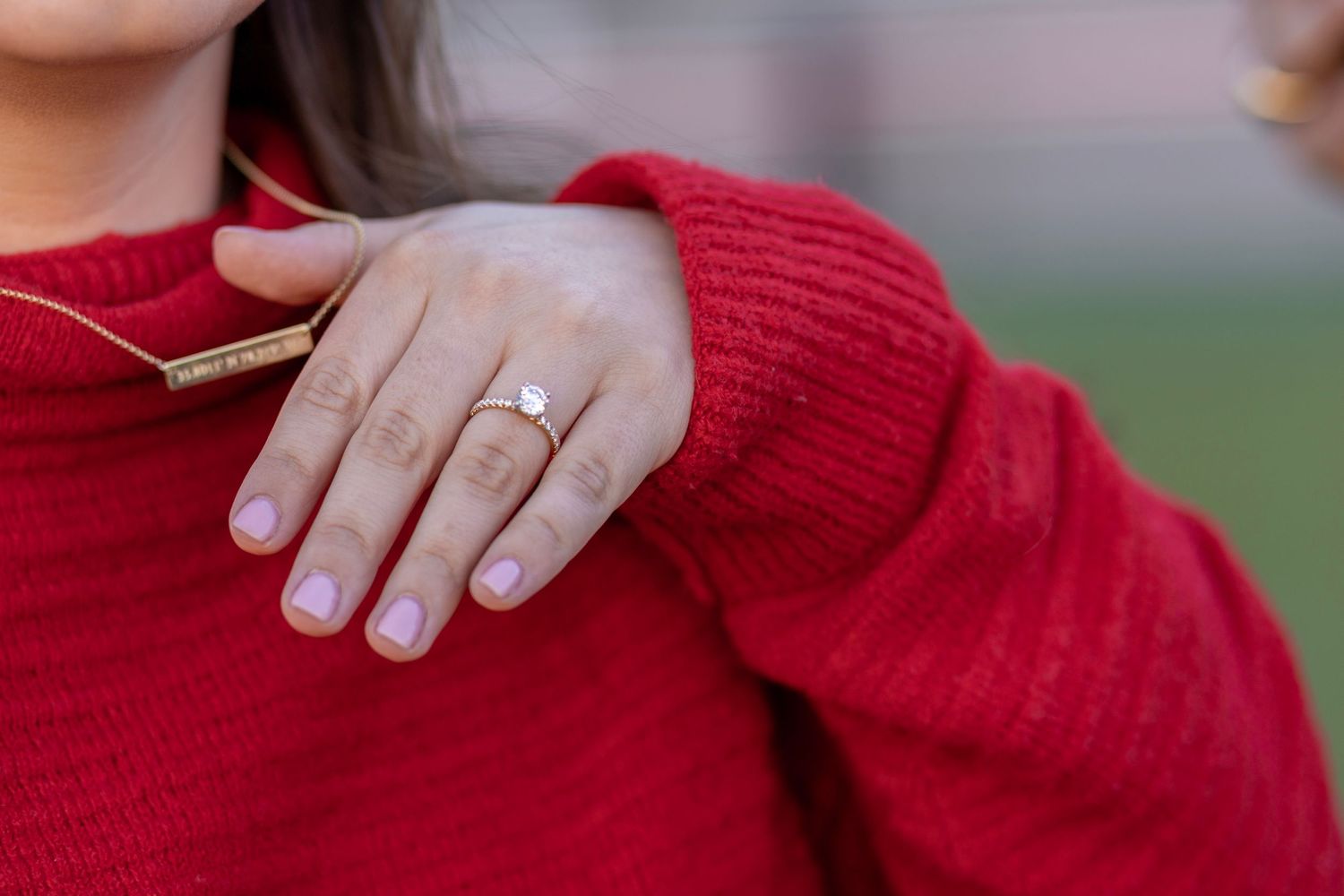 A women displays her coordinate necklace and her engagement ring.