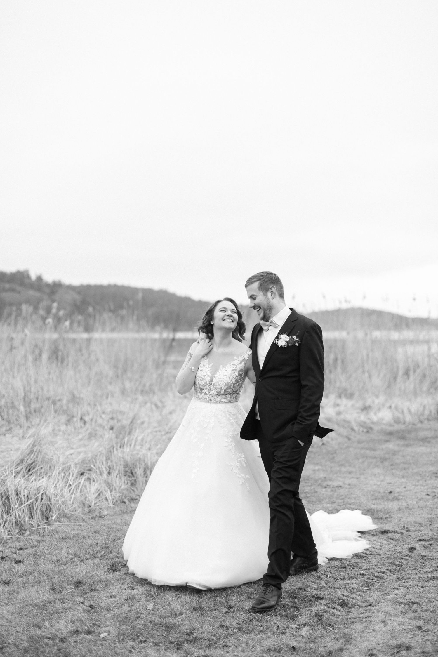 Happy couple laughing together in field during black and white wedding portrait session.