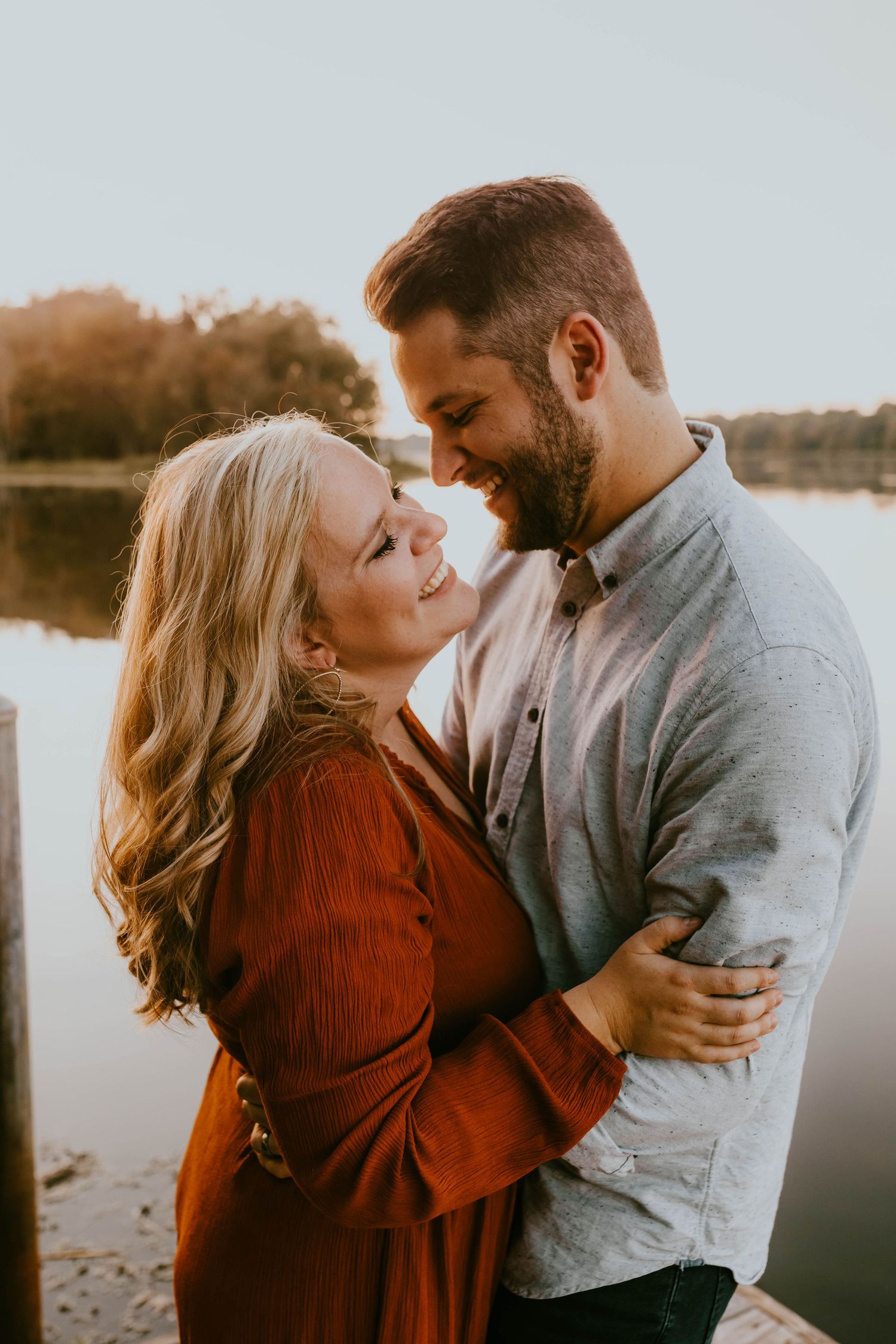 Romantic sunset portrait of couple embracing and smiling by lakeside in autumn attire.