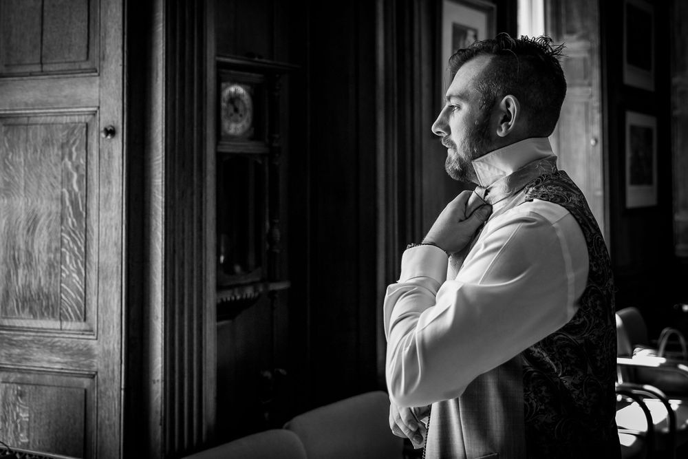 Black and white image of groom adjusting tie while getting ready.