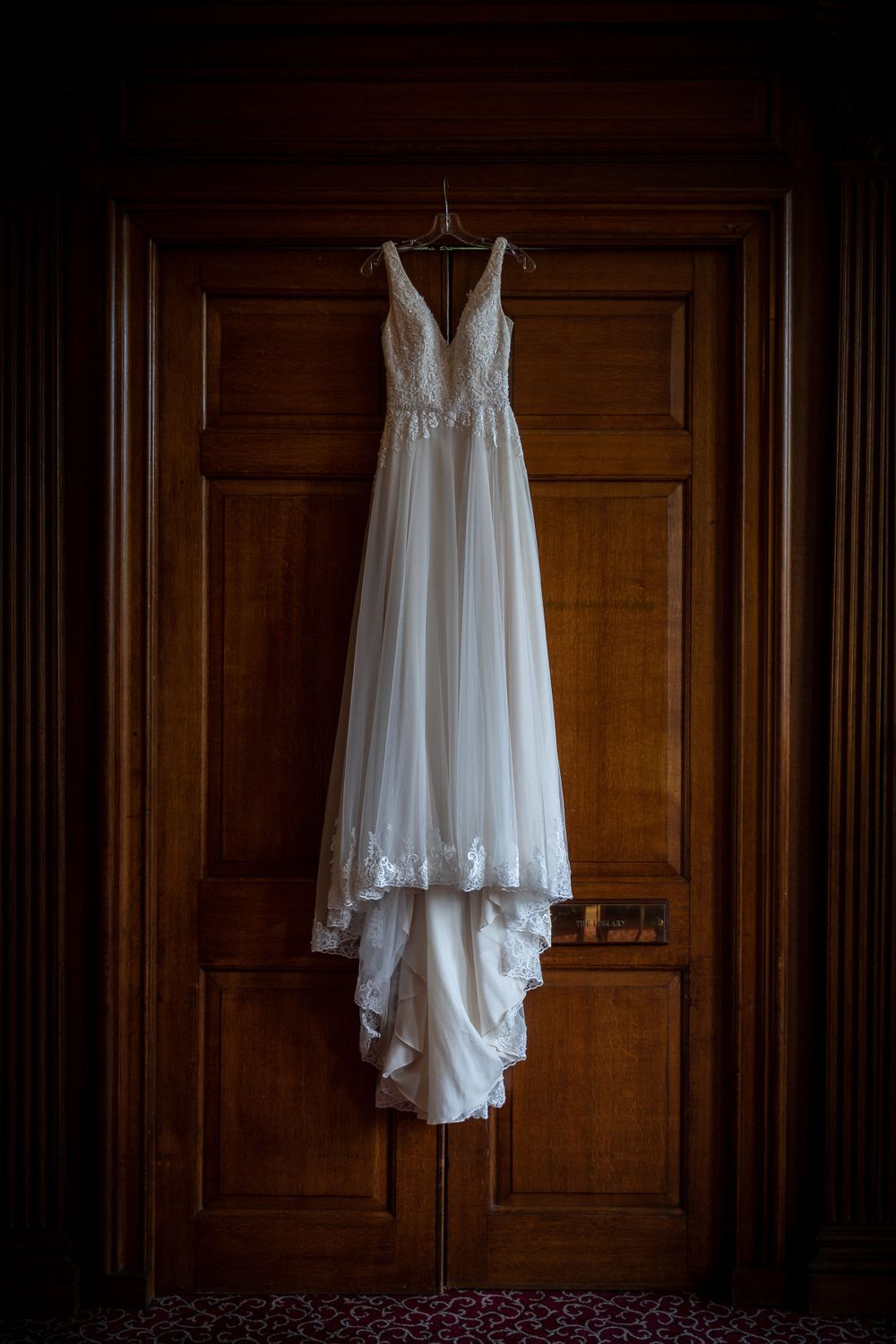Elegant white wedding dress hanging on wooden door in dramatic lighting.