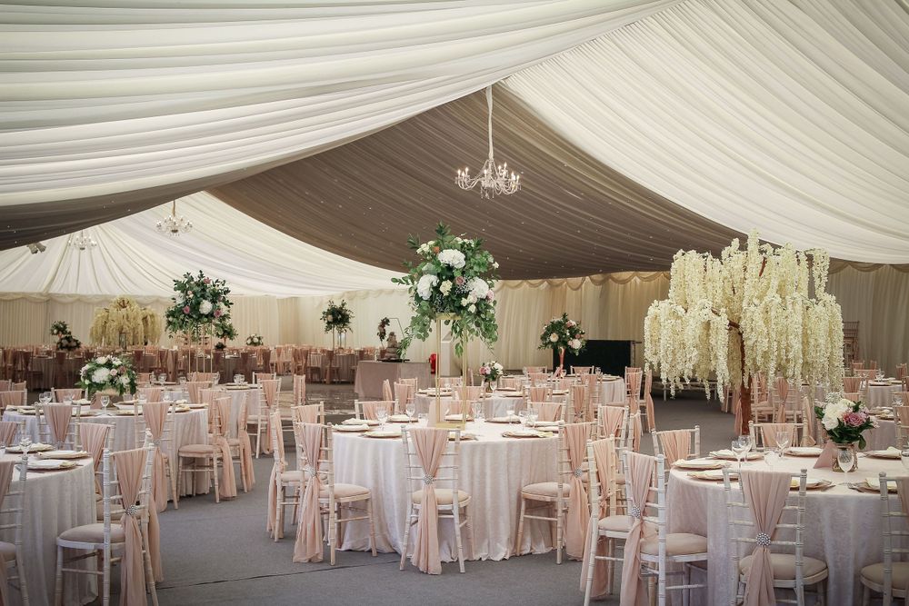 Elegant wedding reception tent with white draping, chandeliers and floral centerpieces.