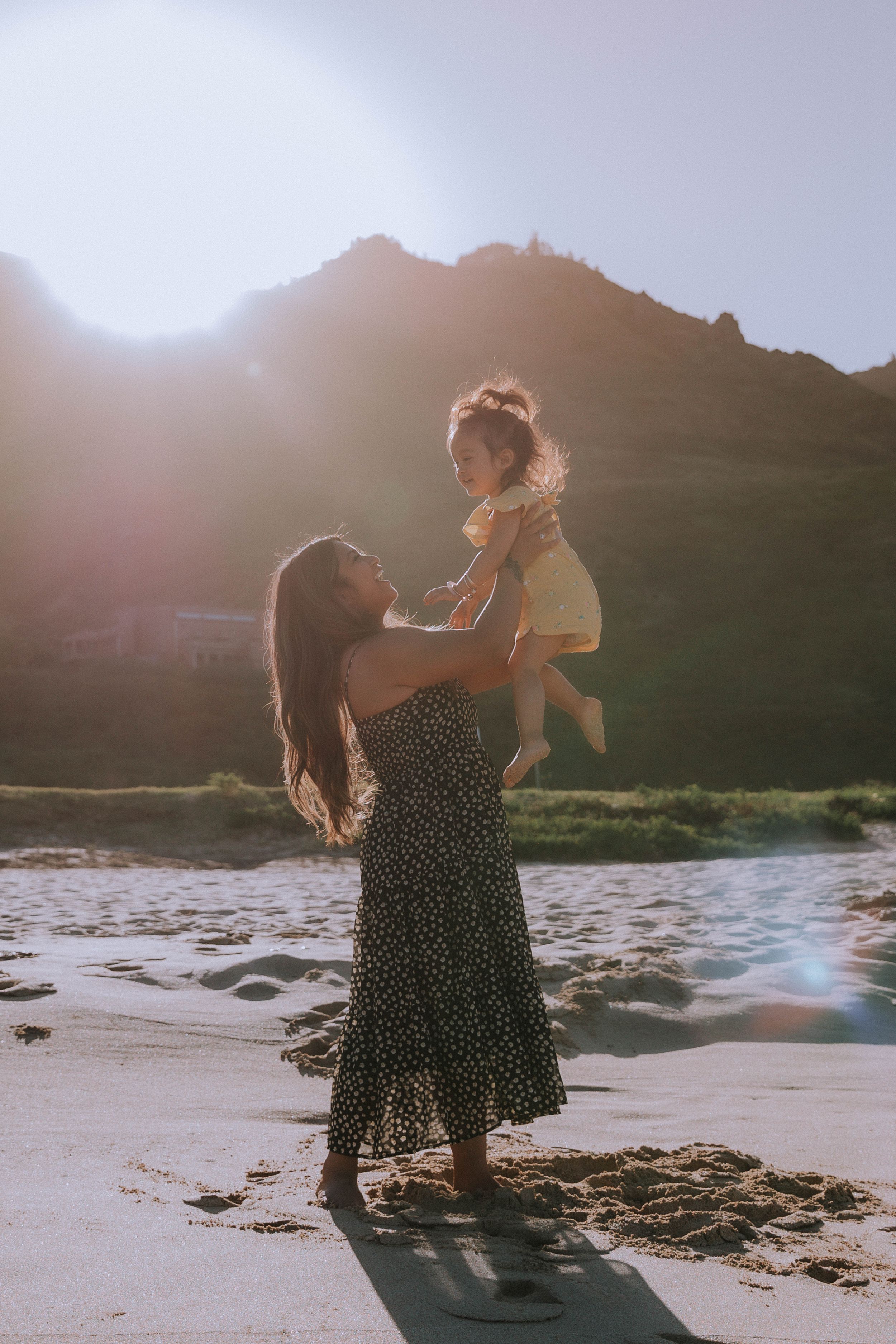Family plays together on beach with mountains and sunset in background.