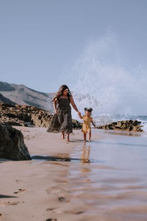 A joyful beach scene with waves crashing as figures play along the sandy shoreline at sunset.