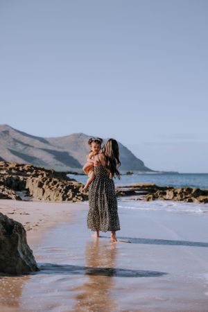 Figures wade in shallow beach water with coastal mountains in background.
