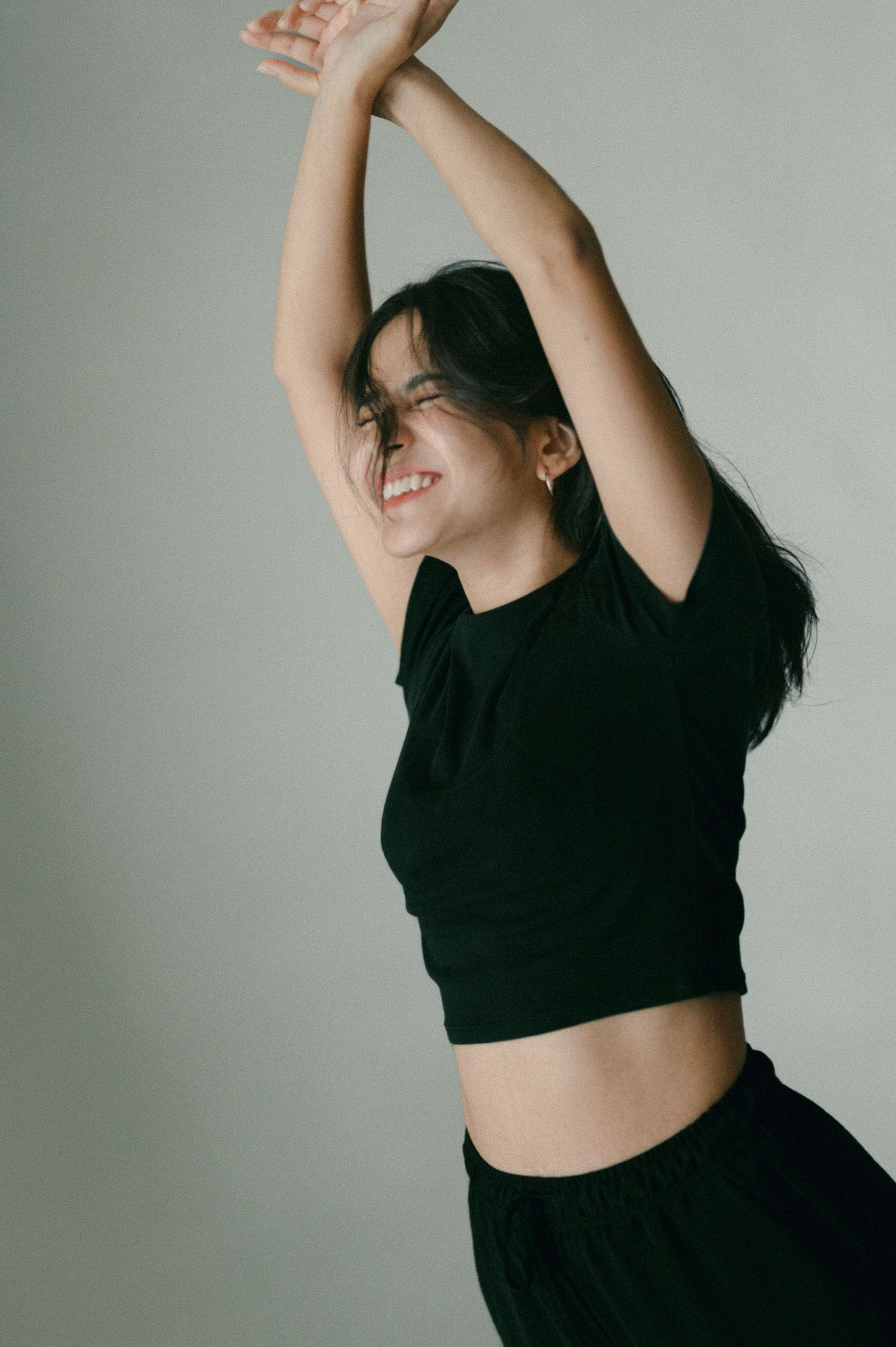 Dance-inspired pose with black outfit against white background showing joyful movement.