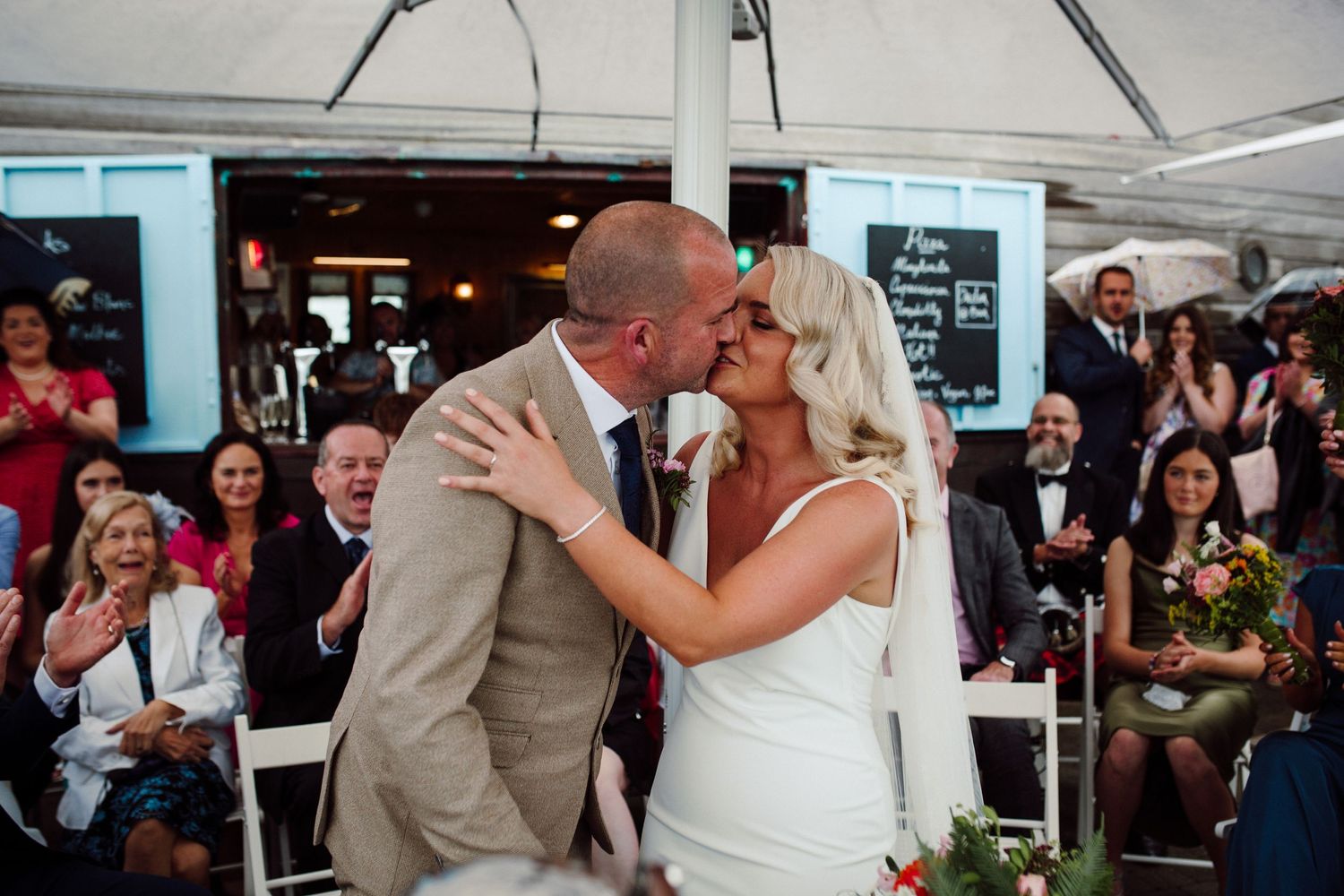 Romantic first kiss moment at outdoor wedding reception.