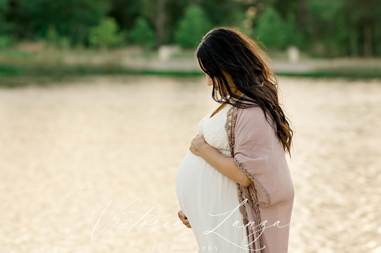 Silhouetted side view of expectant mother in cream dress against golden light.
