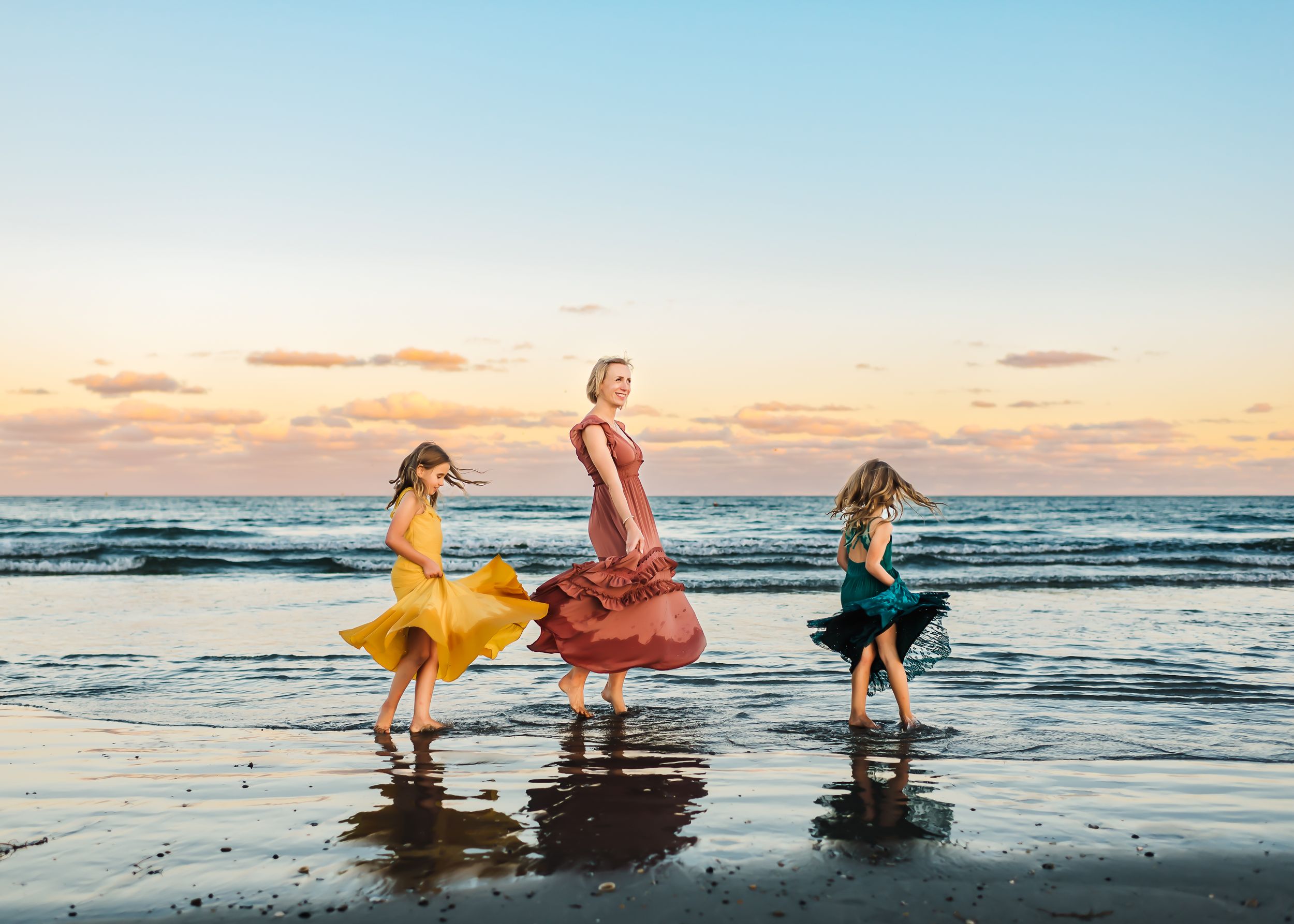 A mom and her two daughter twirling on the beach near Orlando, FL during an outdoor family session.