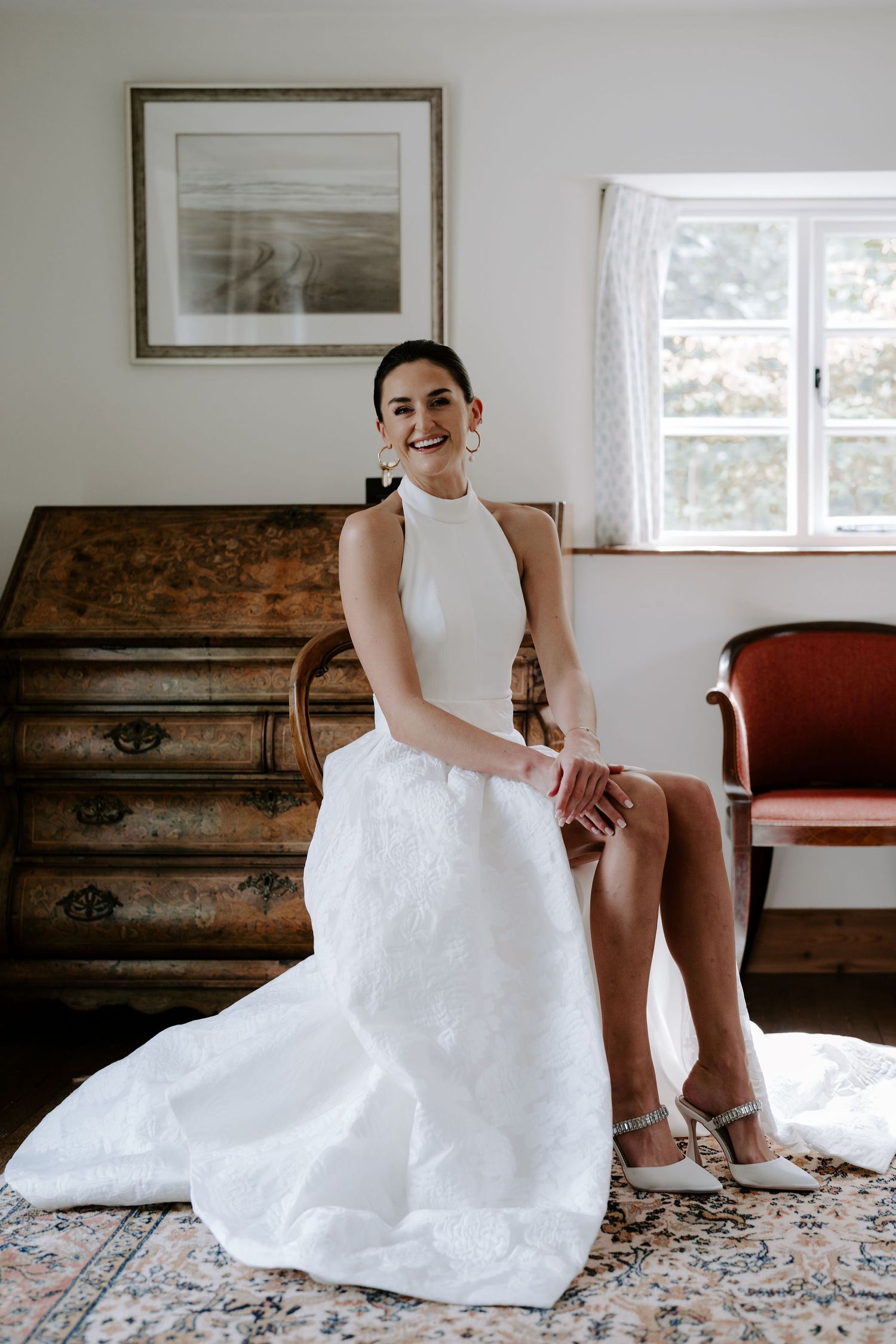 bride sat on chair laughing before she leaves for the church in Oxfordshire