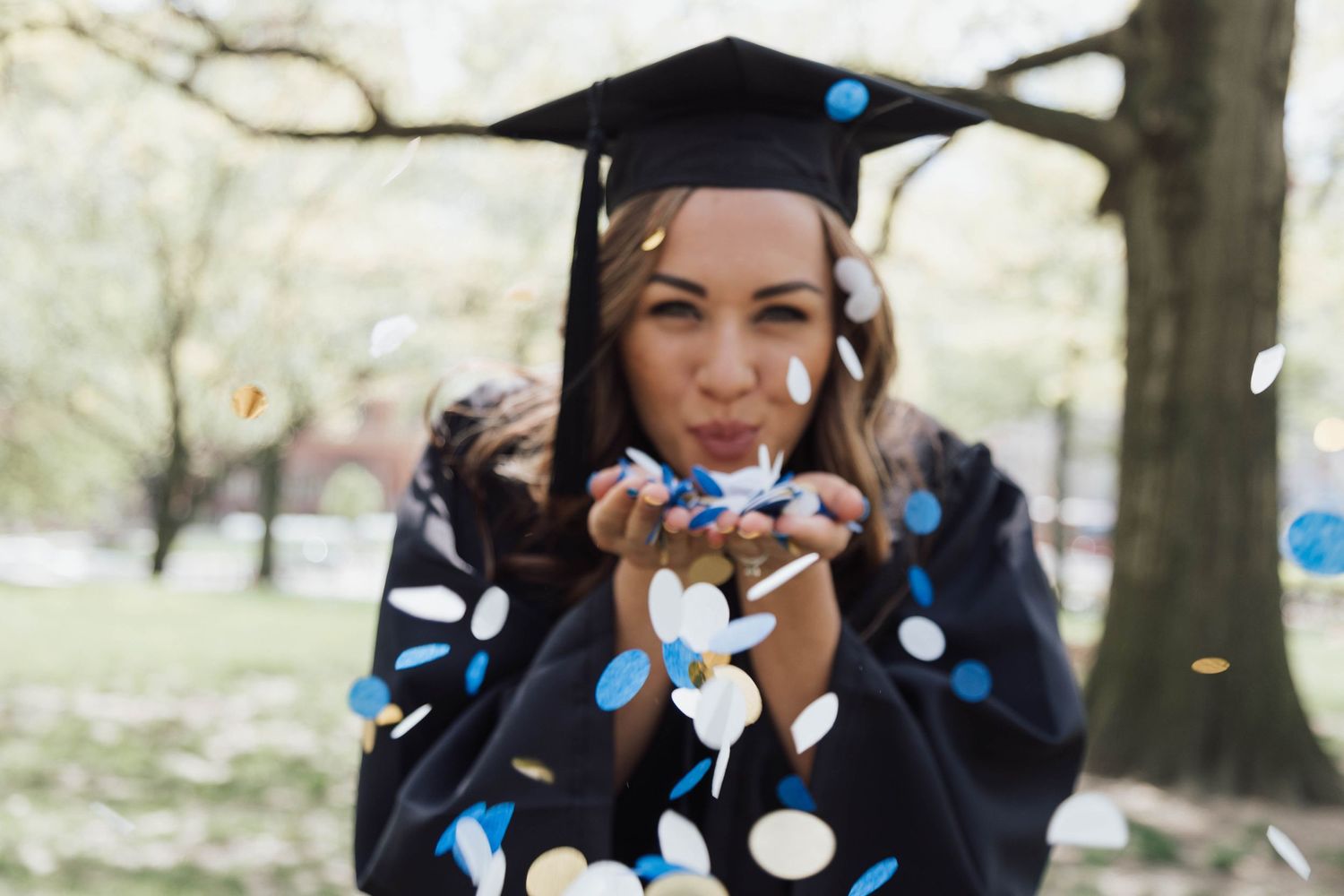 High school senior girl joyfully throwing colorful confetti outdoors