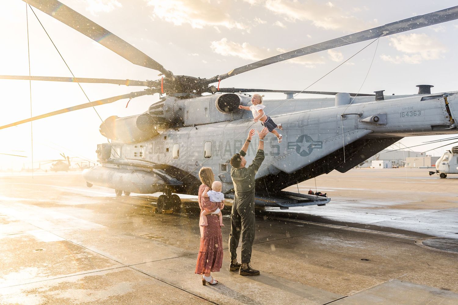 Couple stands together near military helicopter during golden sunset.