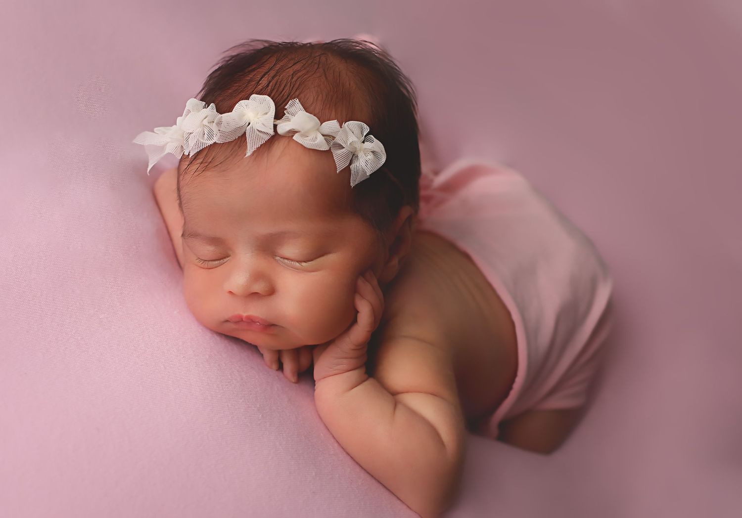Newborn baby girl laying on pink drop on belly posed with hand on chin for newborn session in Alvin, Tx