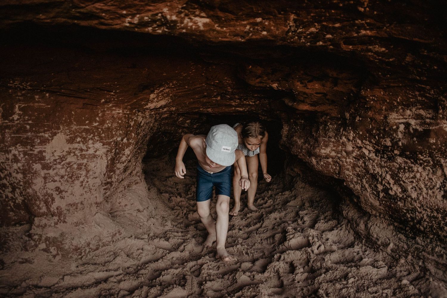 People crawling through a dark cave tunnel during an adventure expedition.