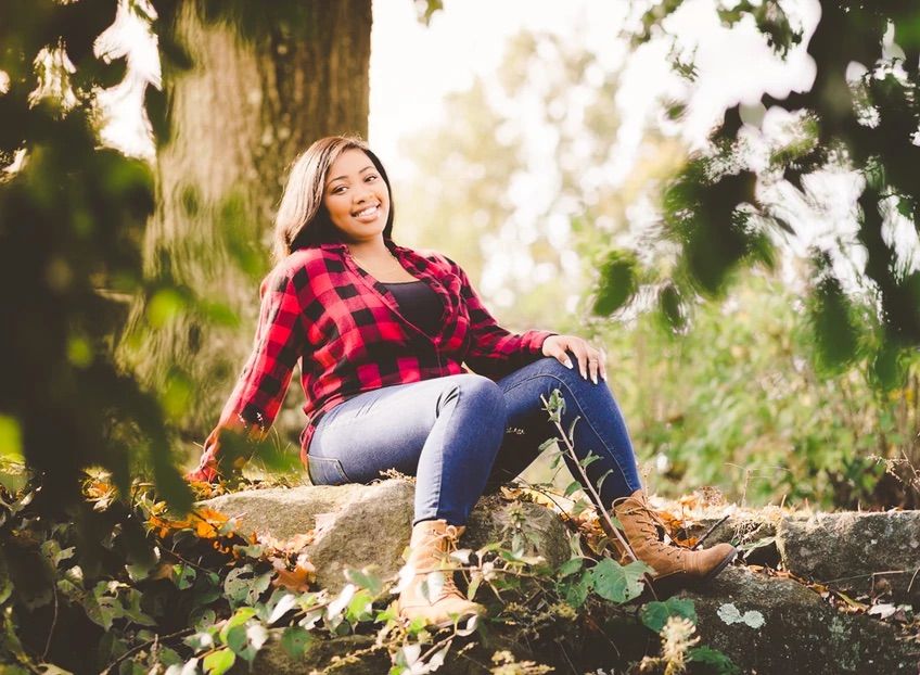 Someone in a red plaid shirt and jeans relaxes outdoors during an autumn photoshoot.