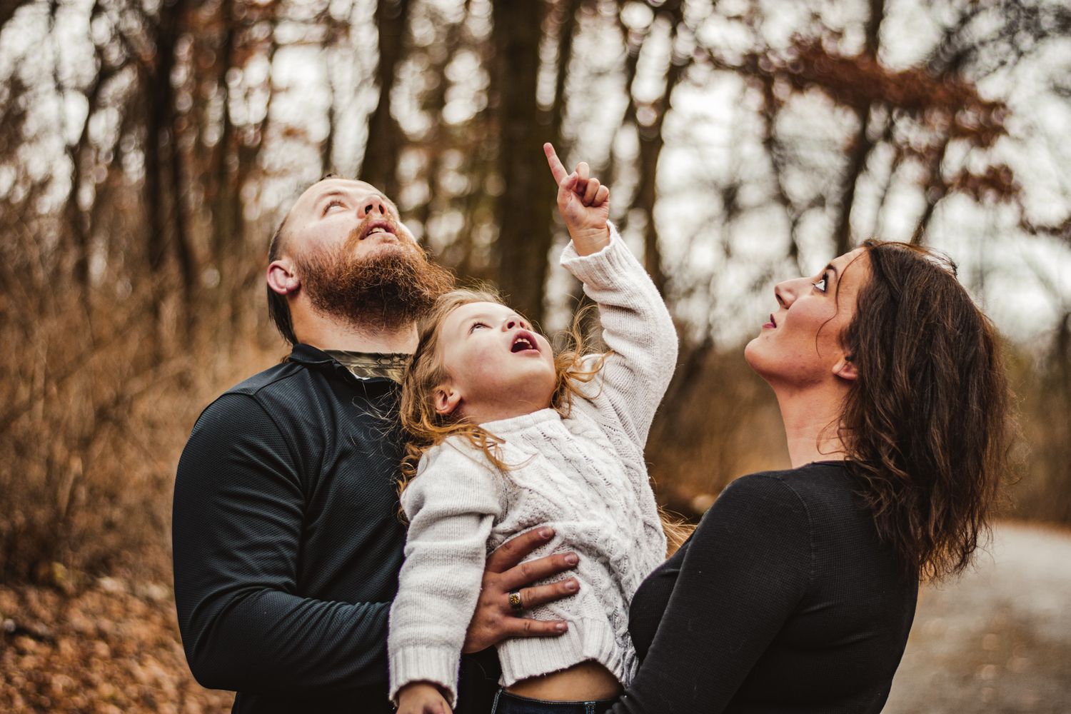 Happy family looking up at sky together in autumn forest setting.