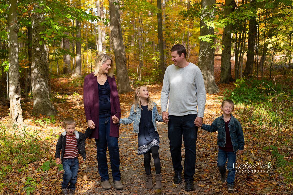 Family of 5 walk together for a fall family photo along a path in a forest in Courtice