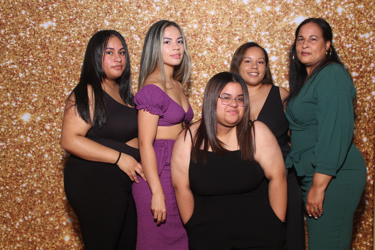 Five friends pose together against a sparkly gold backdrop at a festive celebration event.