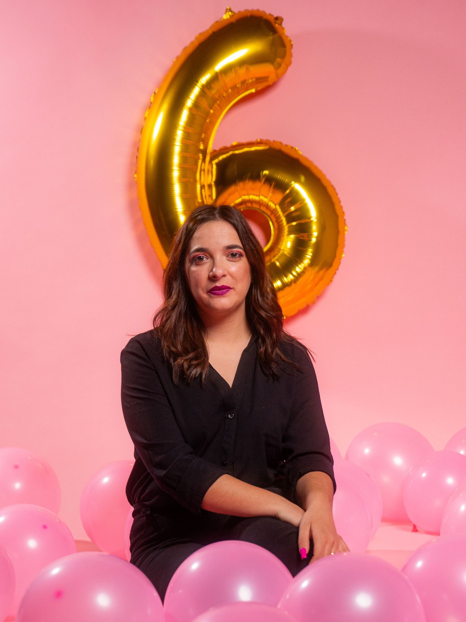 Celebratory photo setup with gold number 6 balloon and pink decorations against rose backdrop.