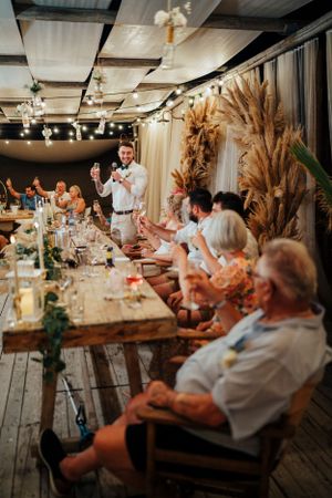 Wedding reception speech in rustic venue with dried pampas grass decor and string lights.