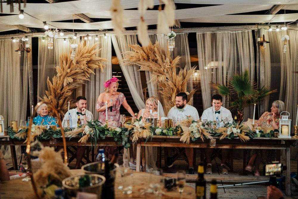 Rustic wedding reception with boho dried grass arrangements and wooden tables.