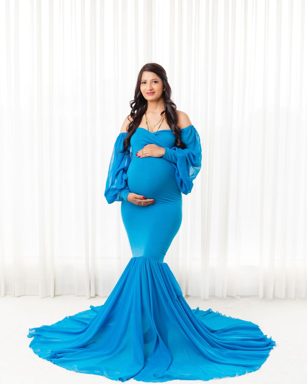 Maternity portrait in a dramatic turquoise mermaid dress with off-shoulder design.