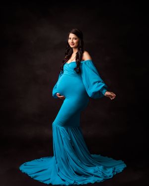 Dramatic maternity portrait featuring a bright blue flowing gown against a dark backdrop.