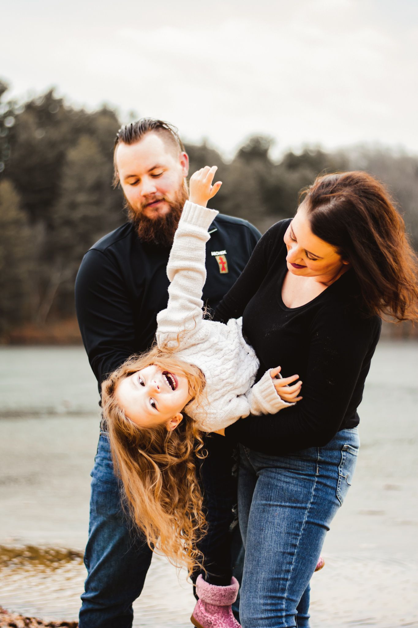 A playful family moment captured by the water on a cloudy day.