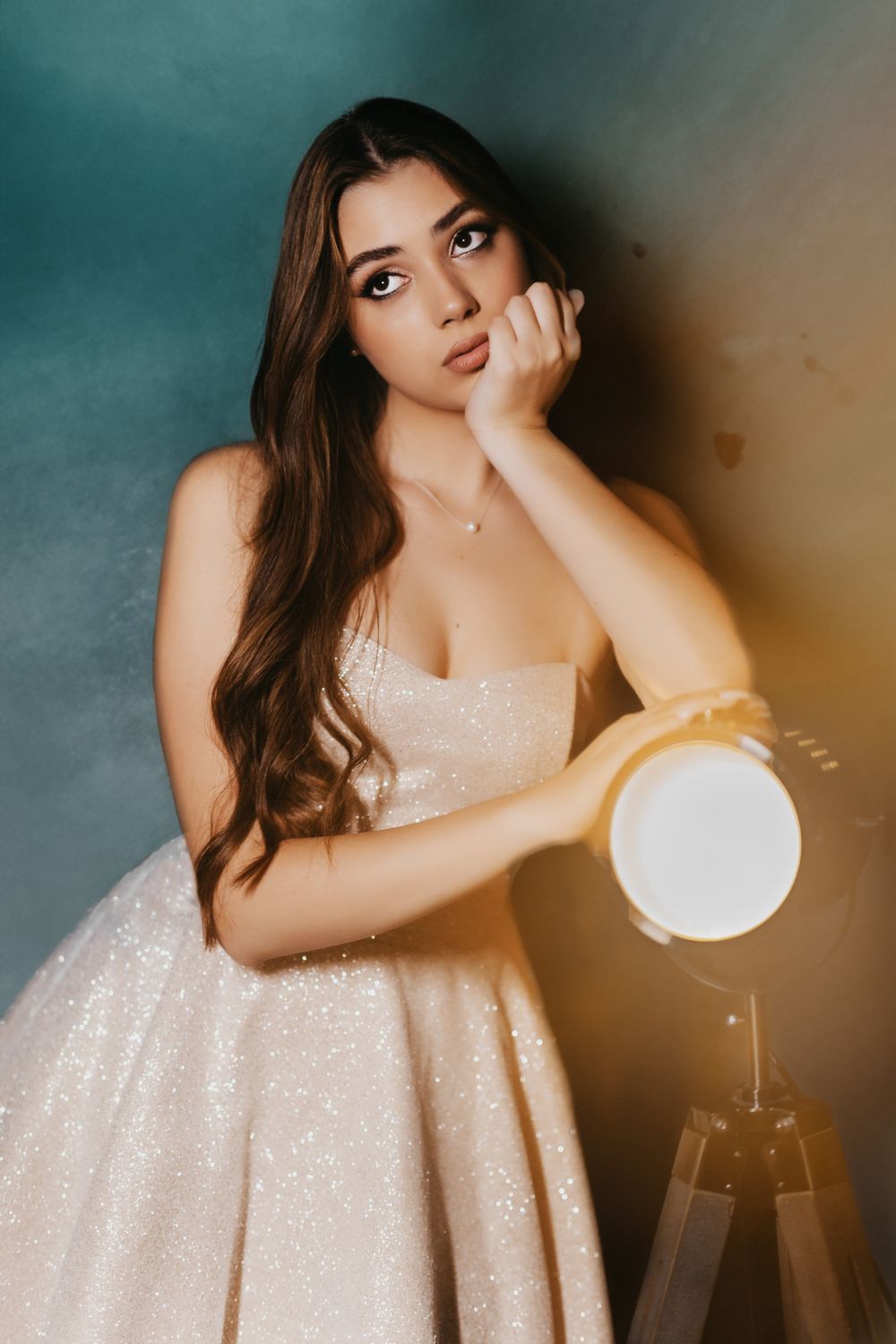 Fashion portrait of model in sparkly white dress against moody backdrop with dramatic lighting.