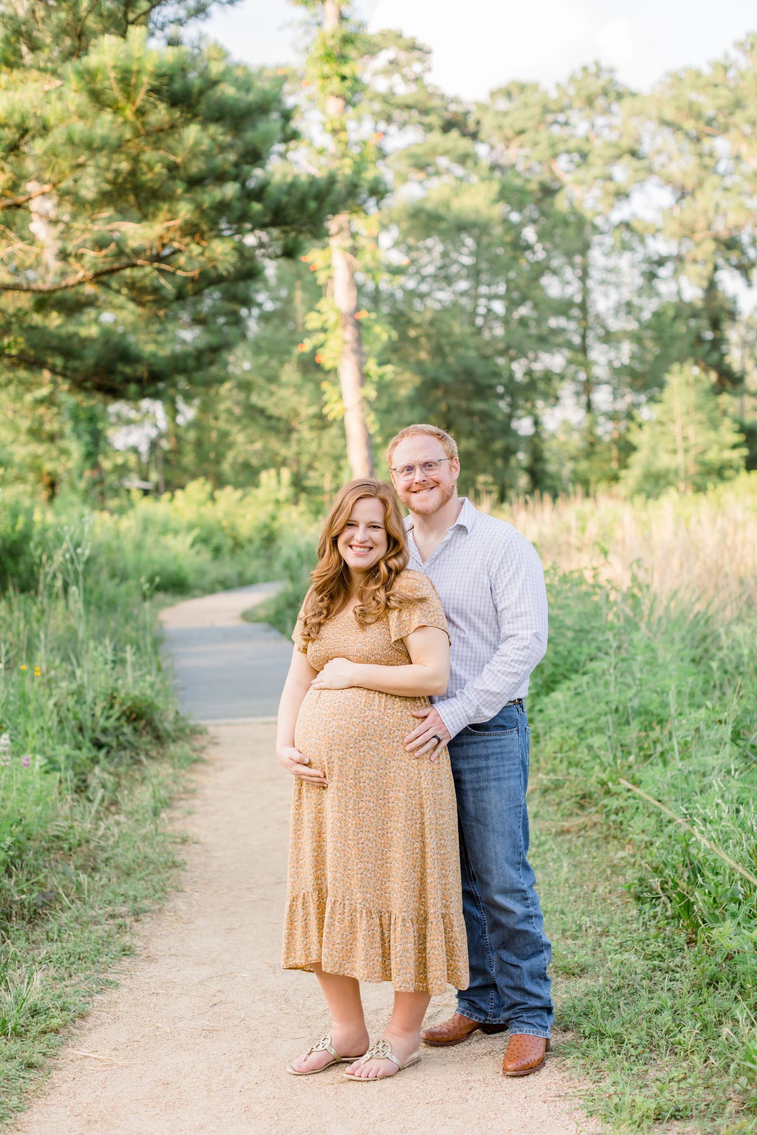 Expecting couple poses together on a nature trail surrounded by greenery.