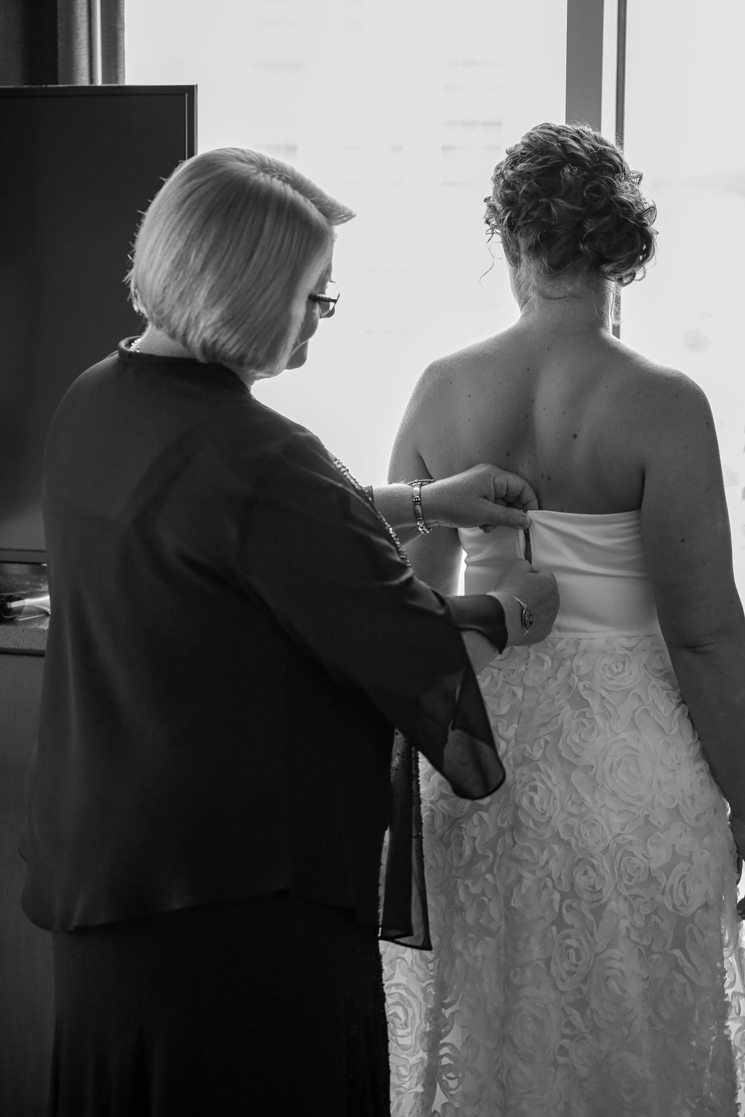 Mom zipping up bride at wedding.