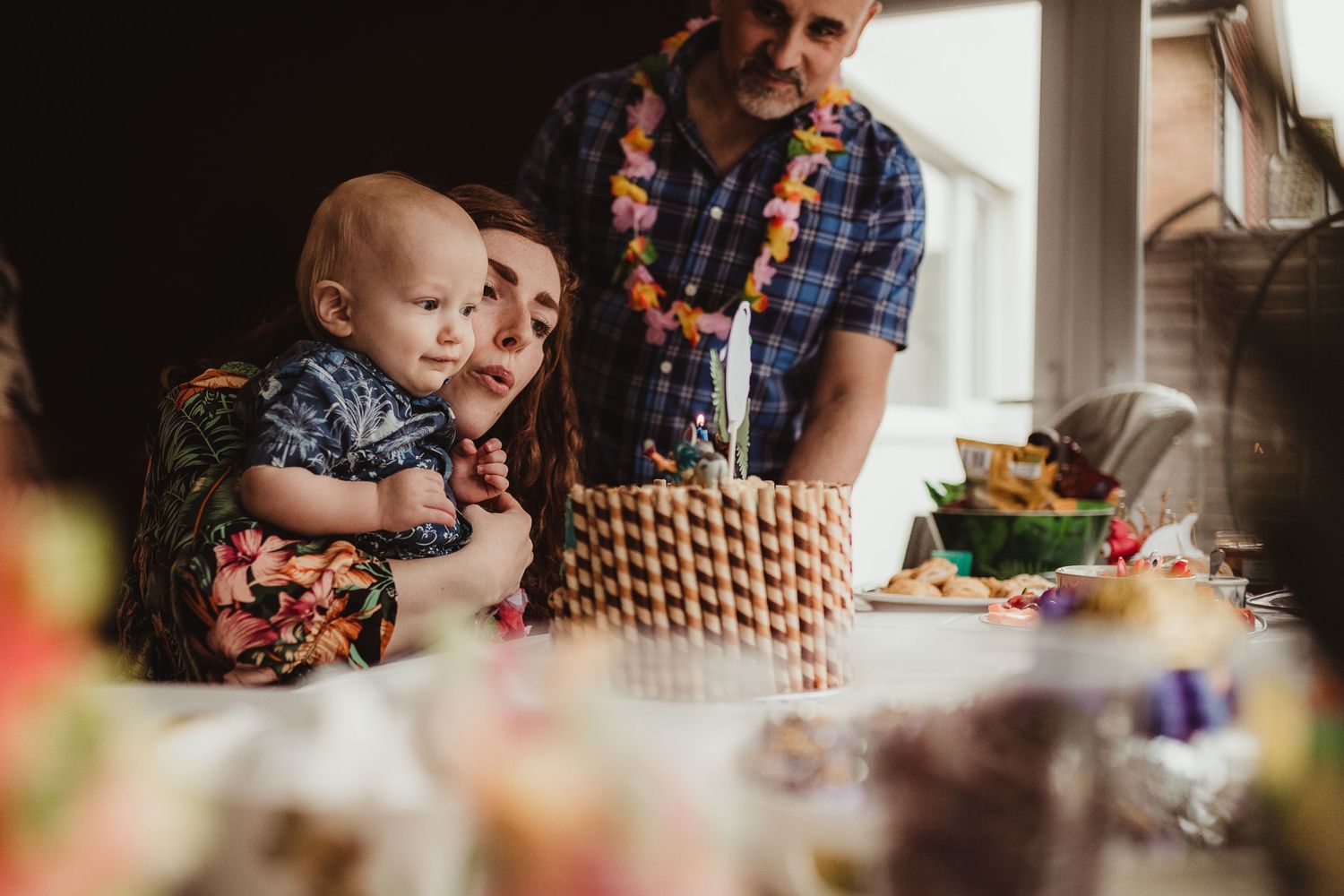 Mummy holding her little boy whilst he blows out the candle on his birthday cake