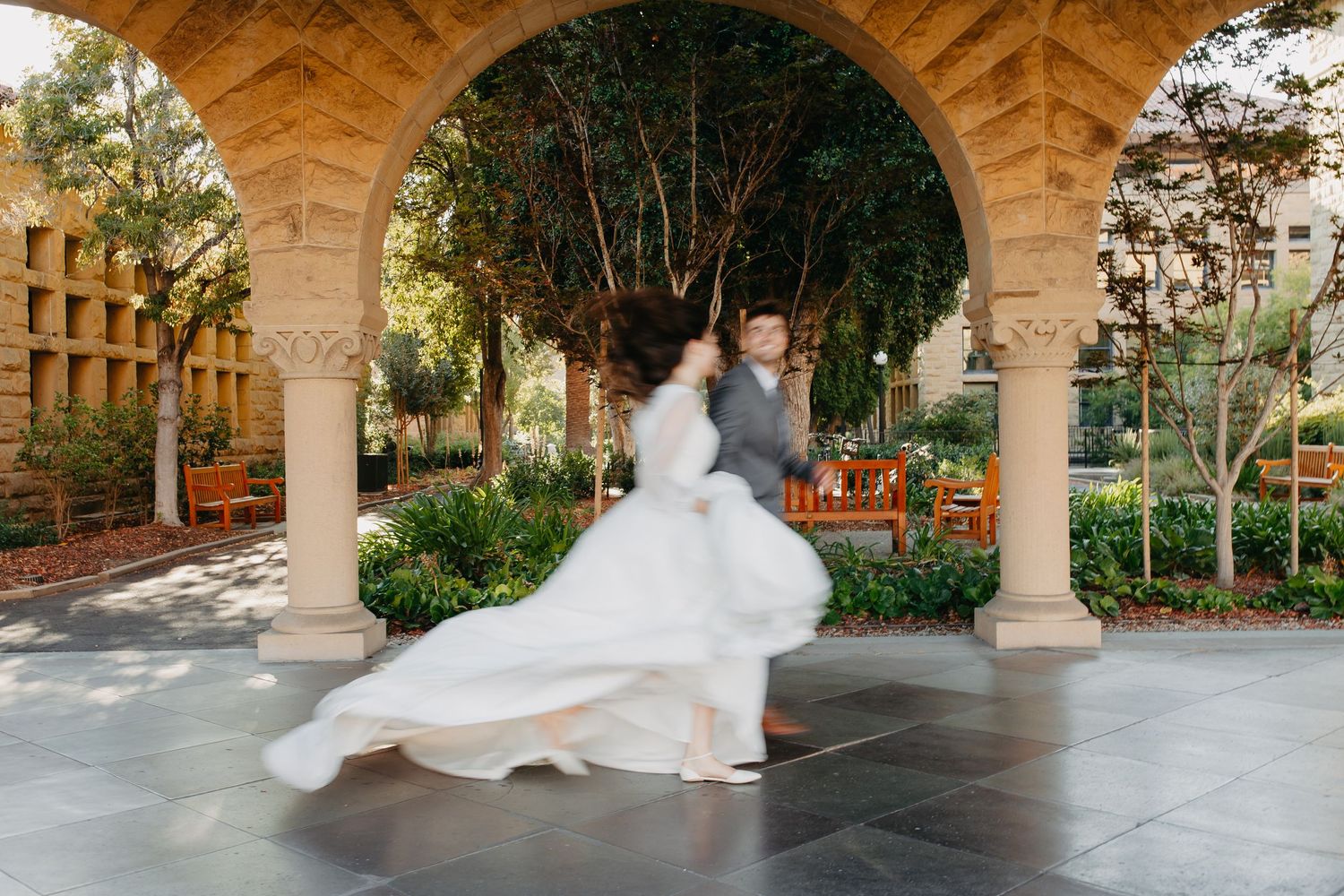 A whimsical wedding photo capturing a flowing white dress twirling under an ornate archway.