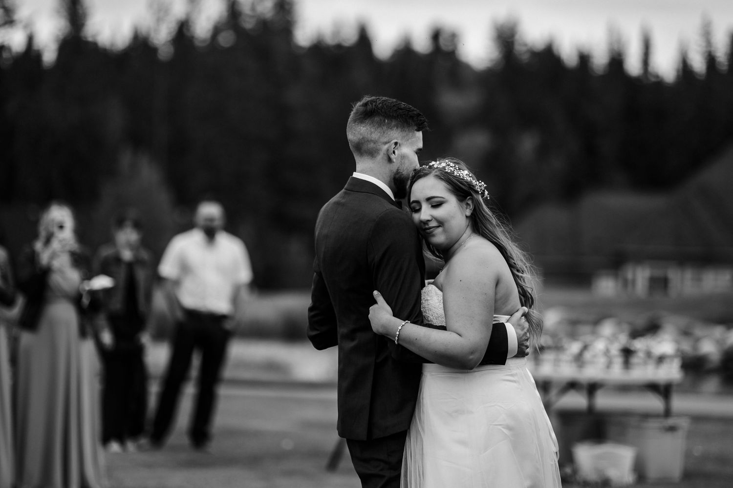 Black and white wedding photo of couple embracing during outdoor celebration.