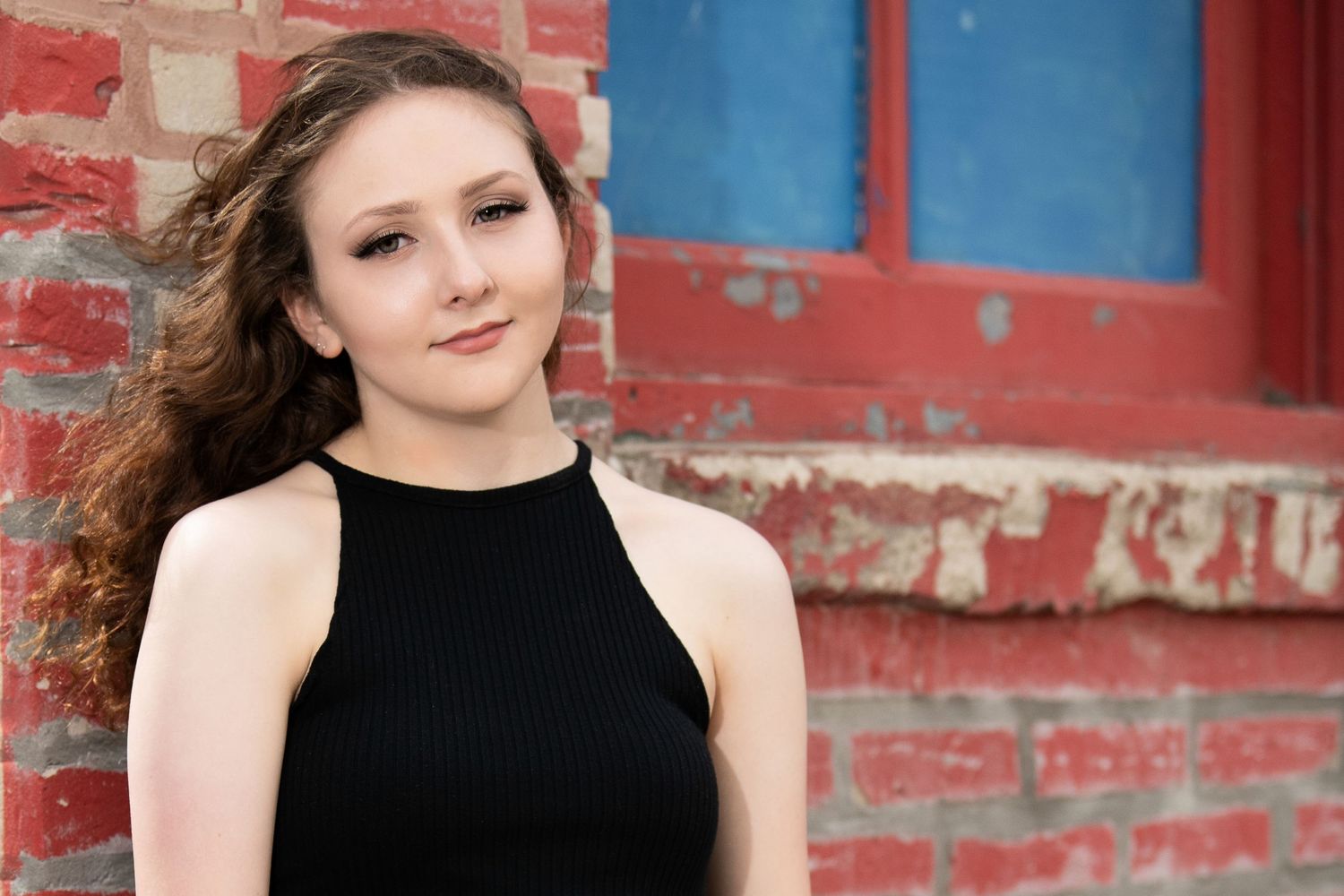 Portrait against red brick wall wearing black halter top with natural lighting.