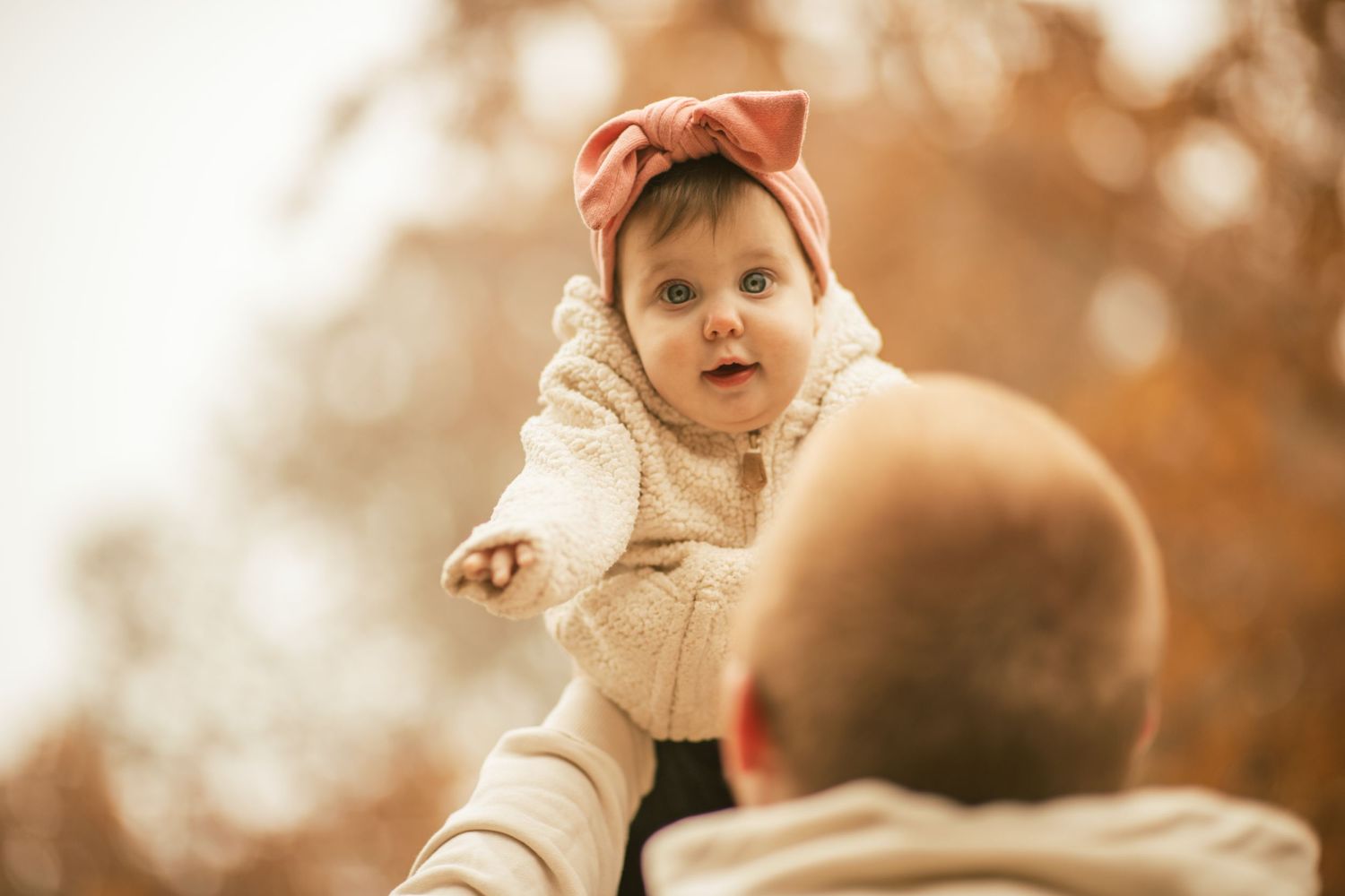 dad holding 1 year old daughter in the air. daughter looking and smiling at camera. fall season