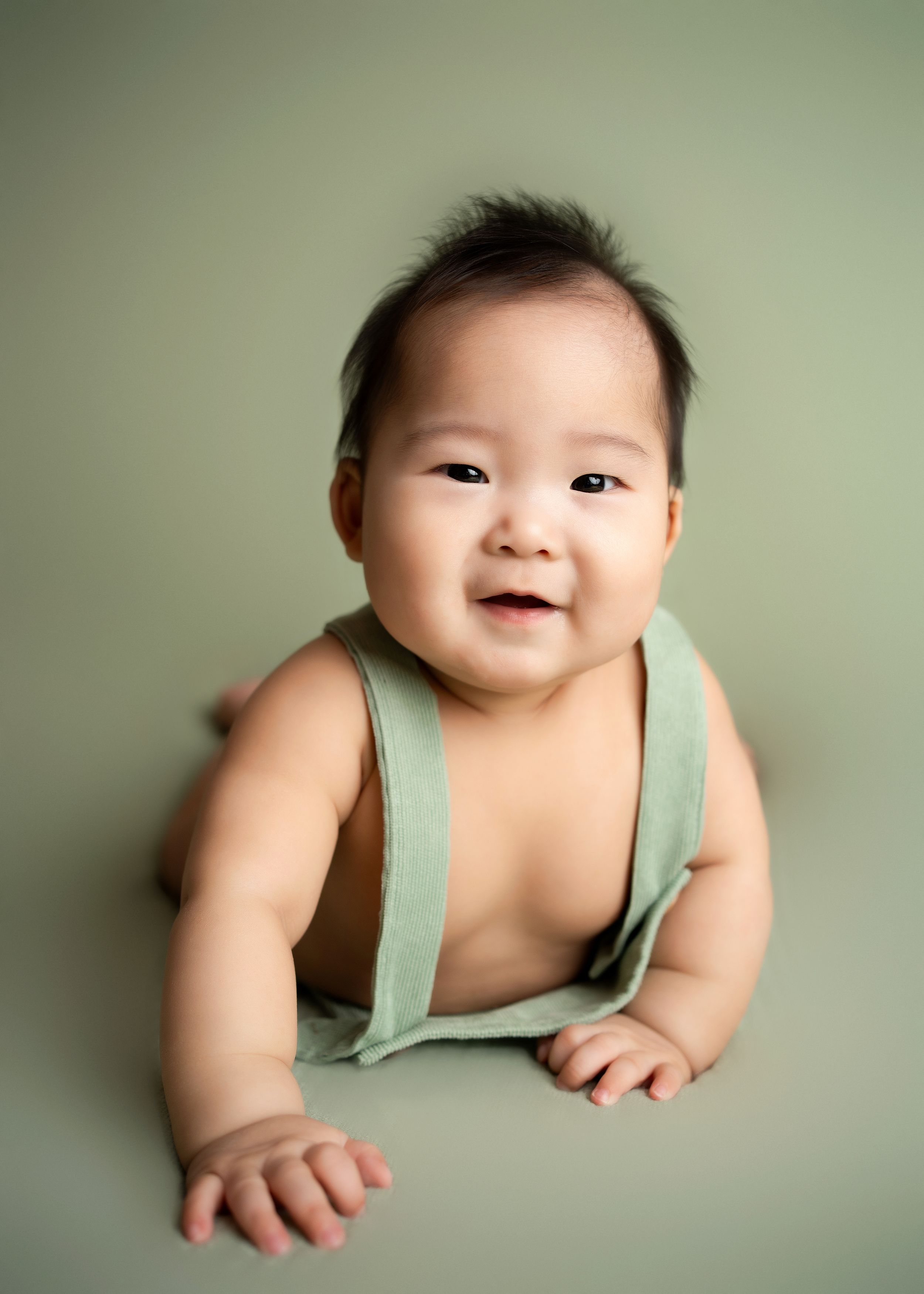 a young boy lays on a light green studio backdrop for a milestone photographer