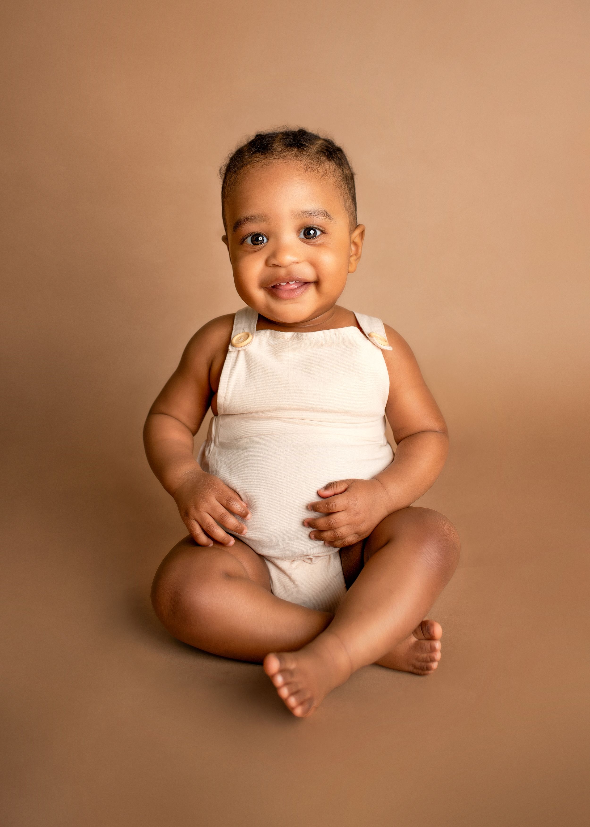 a young boy smiles in front of a brown backdrop for a milestone photographer