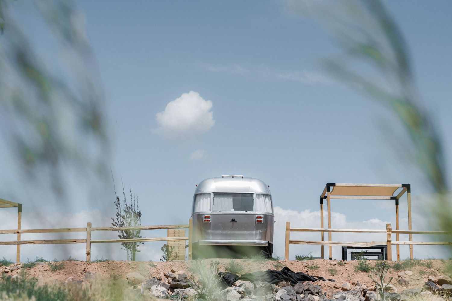 Vintage camper trailers parked along a rural fence line against a blue sky.
