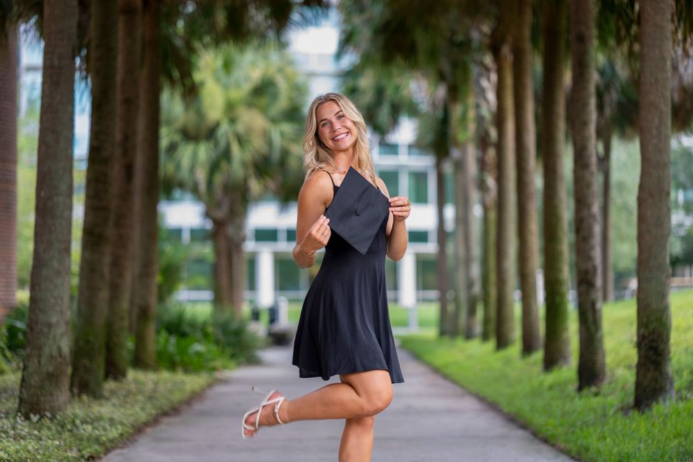 A dancer in a black dress poses gracefully on a tree-lined path.