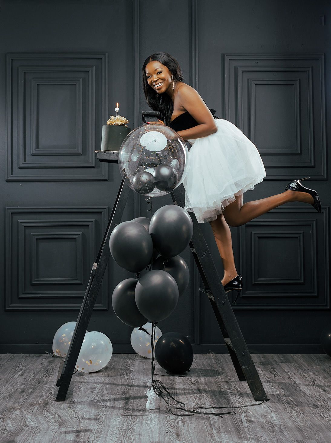 A playful studio portrait with black and white balloons against dark paneled walls.