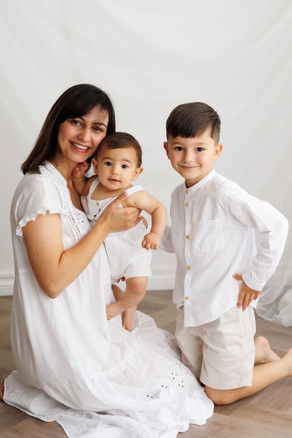 Family in coordinating white outfits poses together for indoor portrait session.