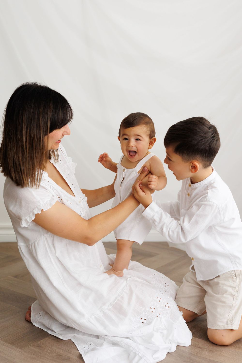 Family sharing joyful interactive moment during white-themed photo session.