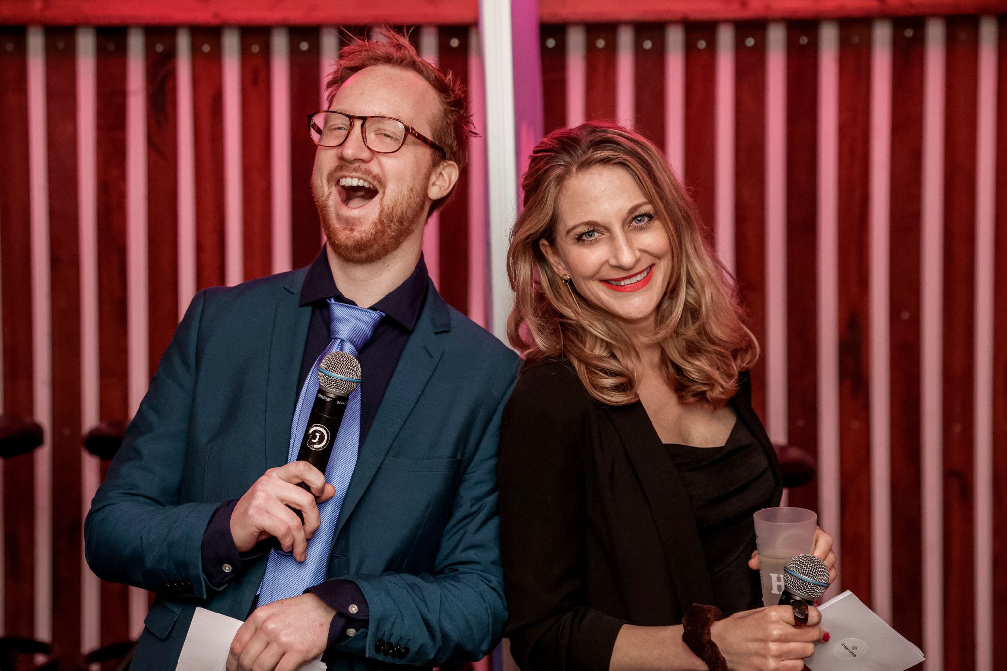Couple laughing together against red striped wall at social gathering.