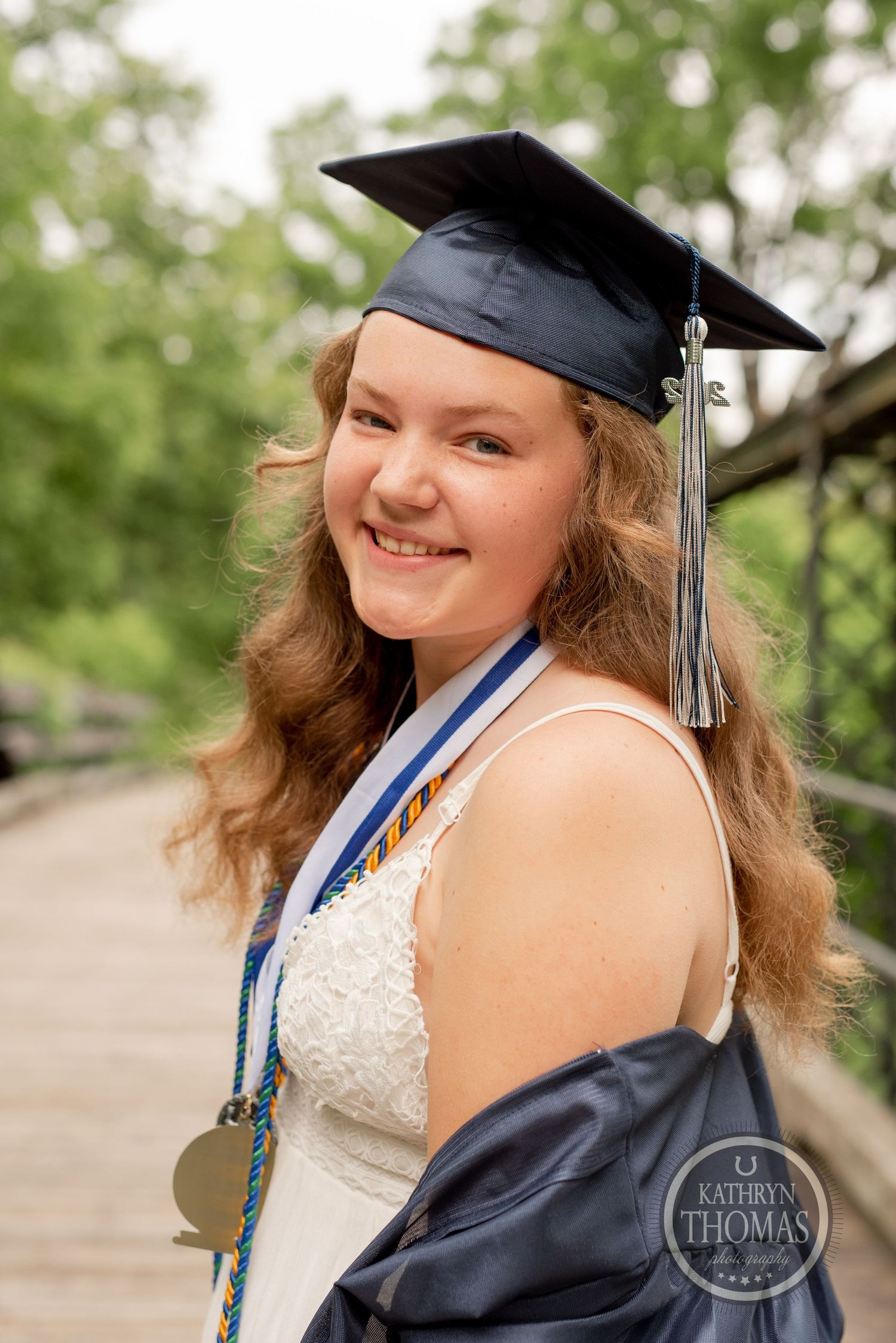 Graduate wearing cap with tassel and medal smiles during outdoor portrait session.