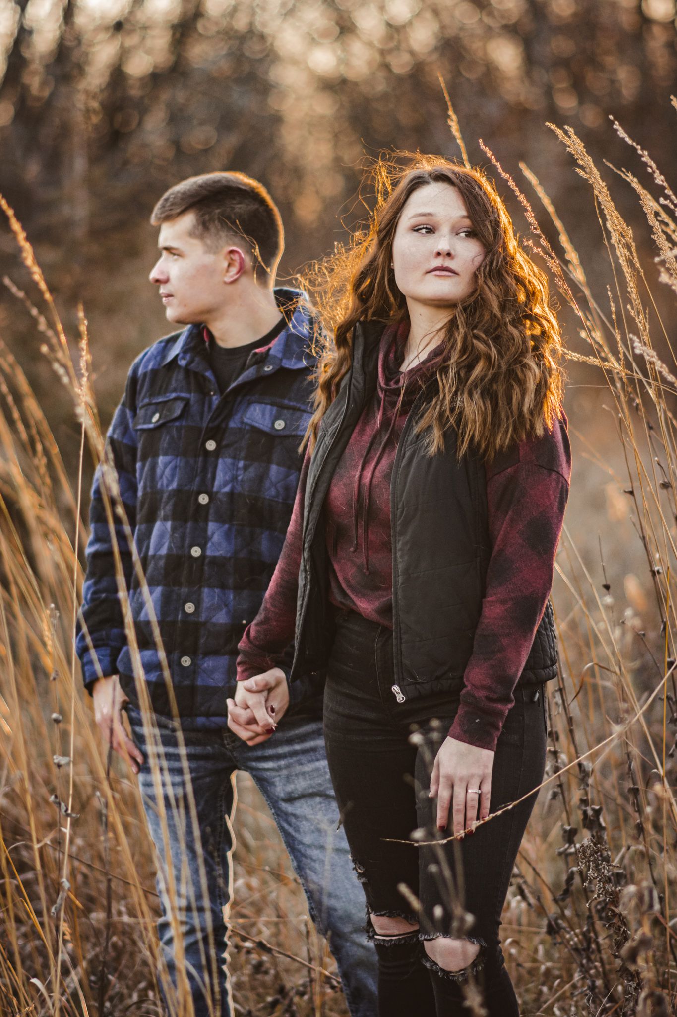 A couple stands together in tall autumn grass during golden hour as sunlight illuminates the scene.