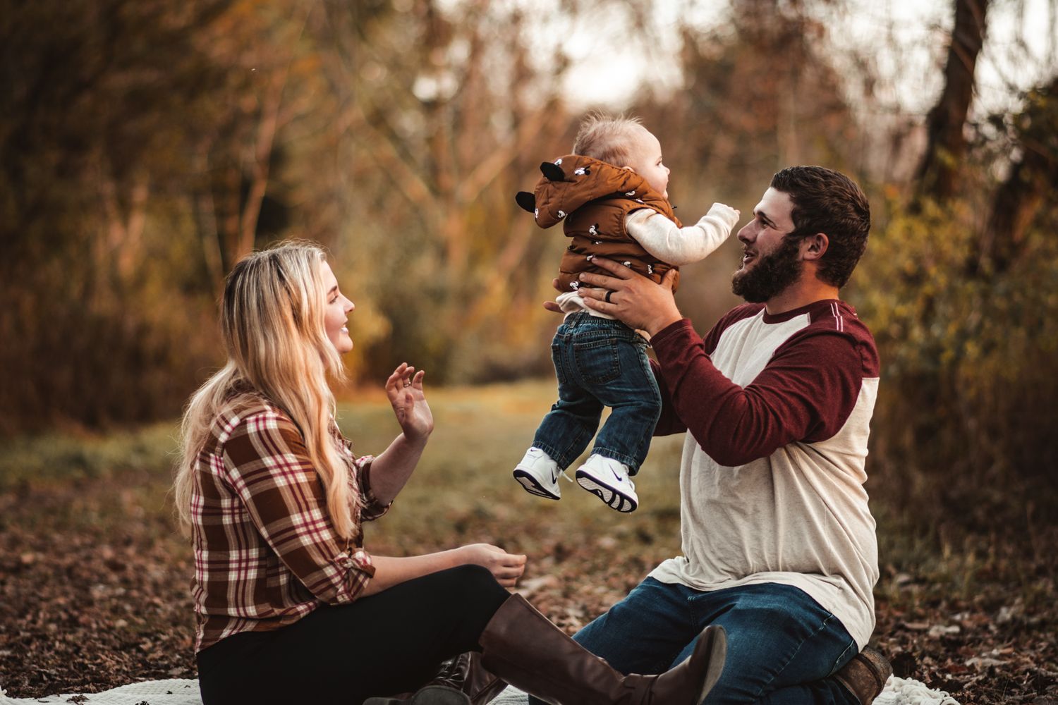 Family plays together outdoors lifting baby in playful moment during fall season.