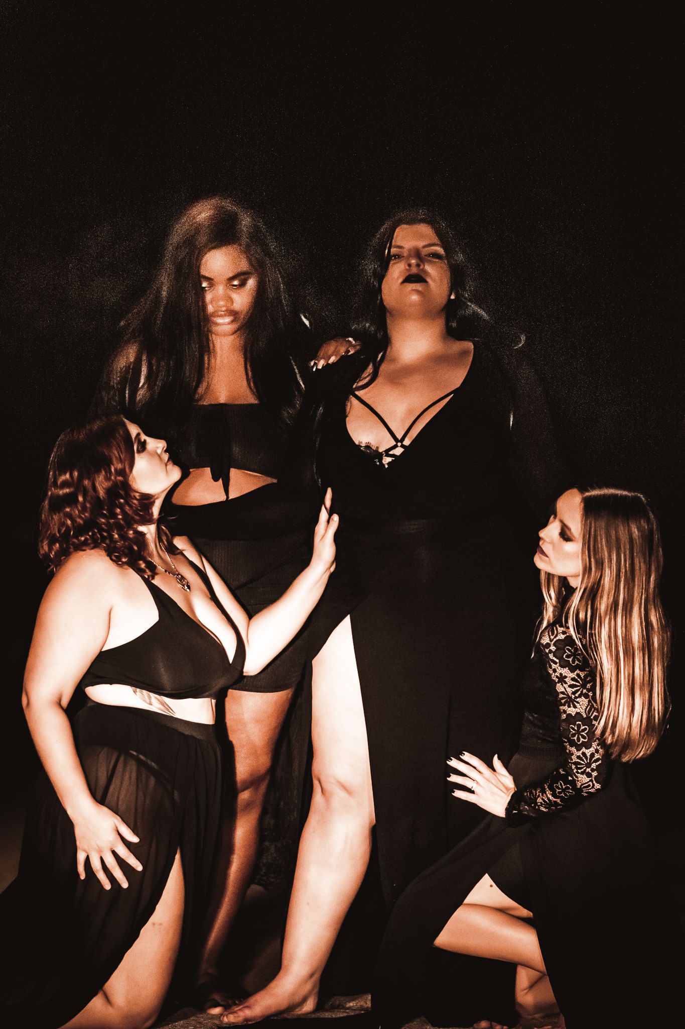 Artistic dark portrait of women in black clothing posing dramatically against dark background.
