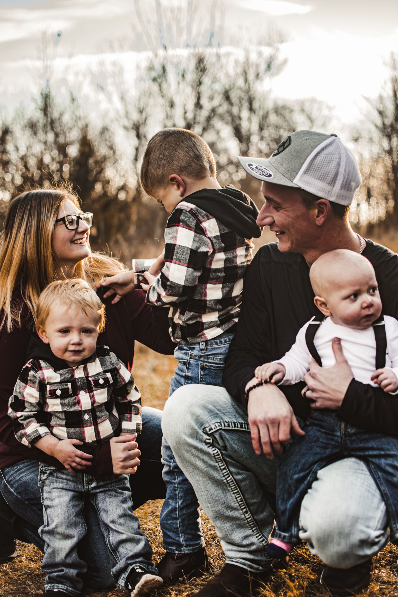 Family sitting together outdoors with young children in matching plaid shirts.