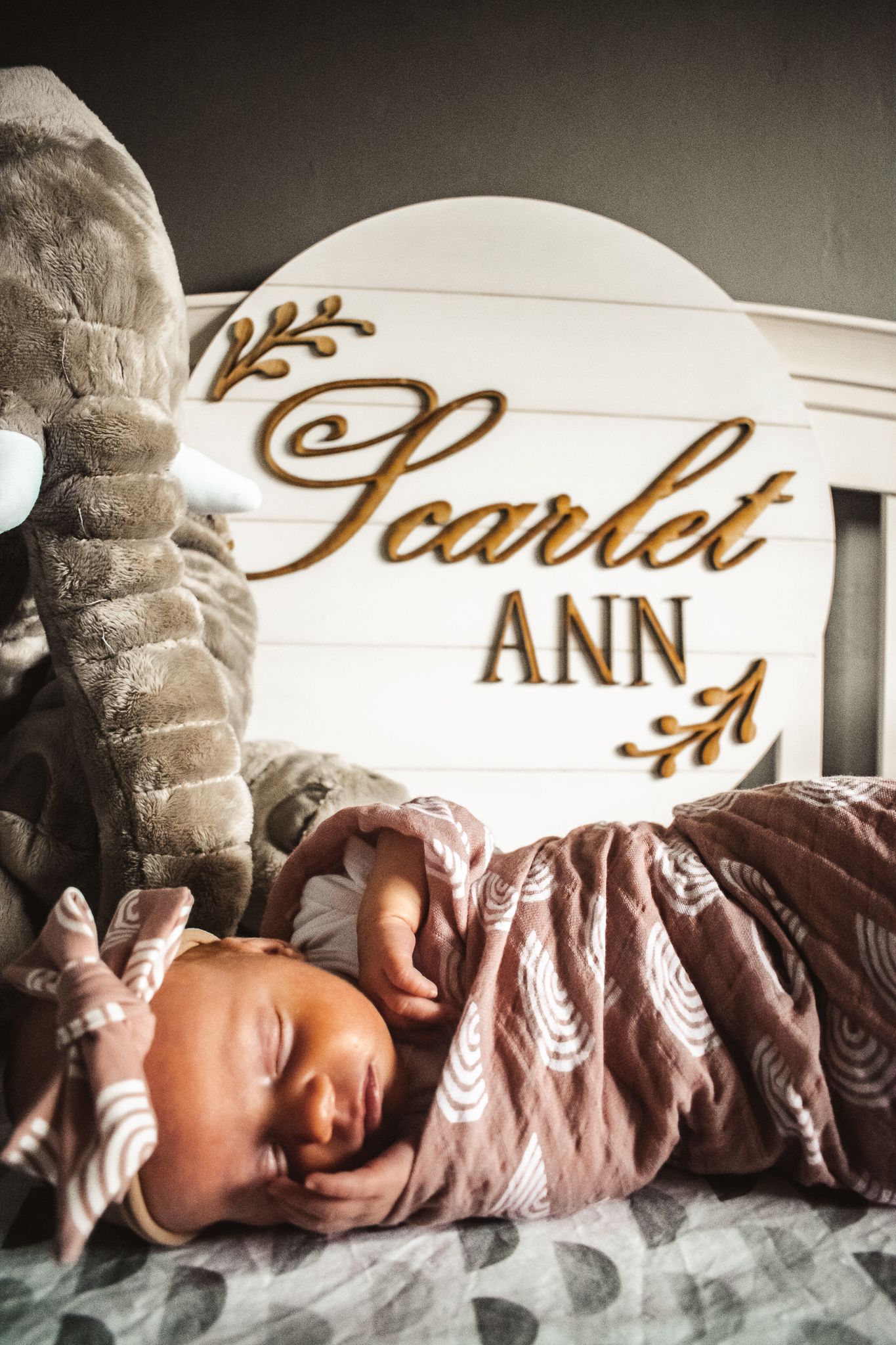 Sleeping newborn baby lying under personalized name sign reading Scarlet Ann.